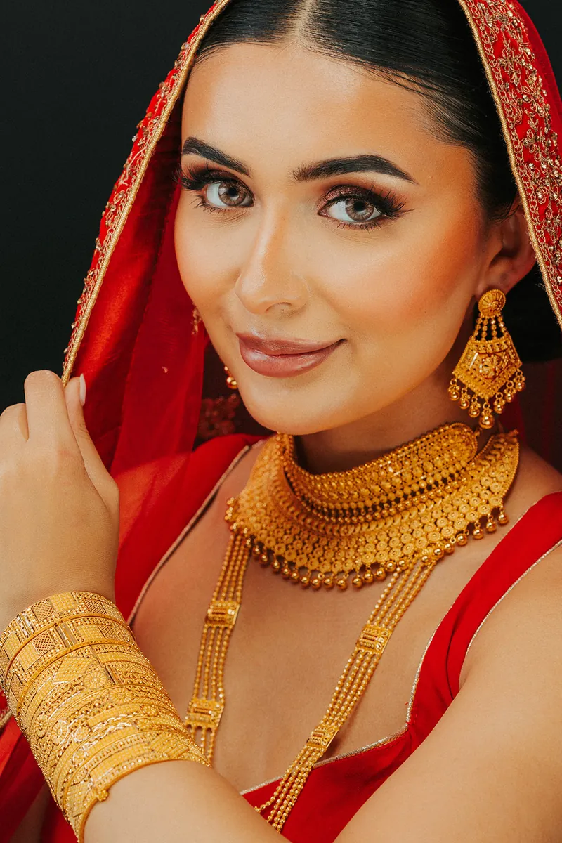 Bride in a red veil wearing a 22k gold choker, necklace and bangles, Sonei Jewellers Surrey