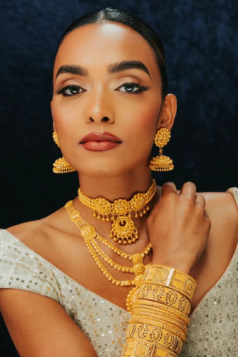 Model in a white outfit wearing layered 22k gold necklaces and bangles, Sonei Jewellers Surrey